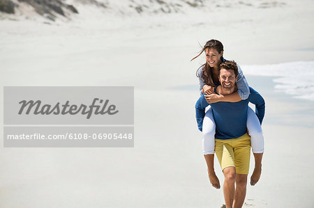 Man giving piggyback ride to his wife on the beach
