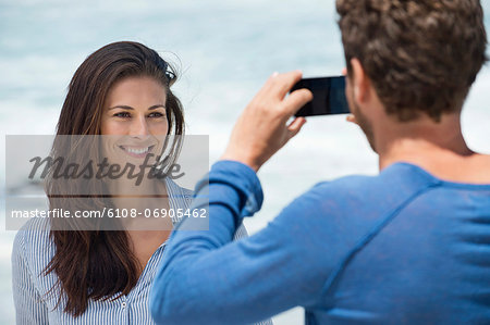 Man taking a picture of his wife with a cell phone on the beach