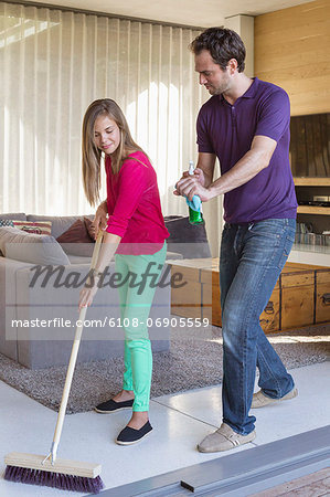 Girl cleaning floor with a mop beside her father