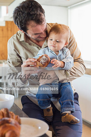 Man feeding bread to his son at a kitchen counter
