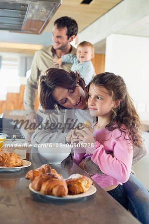 Girl having breakfast beside her mother at a kitchen counter