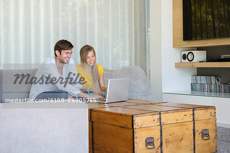 Man and his daughter sitting on a couch looking at a laptop