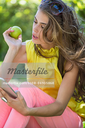 Woman holding an apple and looking at a digital tablet