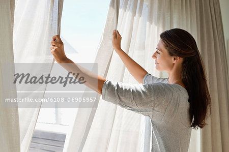 Woman opening the curtain of a window Woman opening the curtain of a window