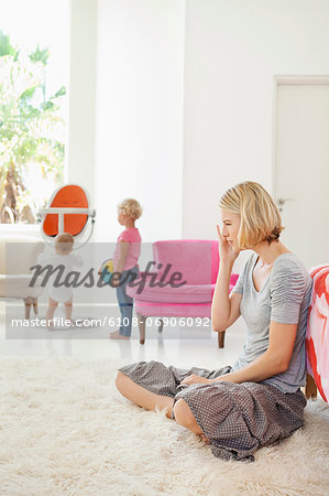 Woman sitting on a rug with her children playing in the background