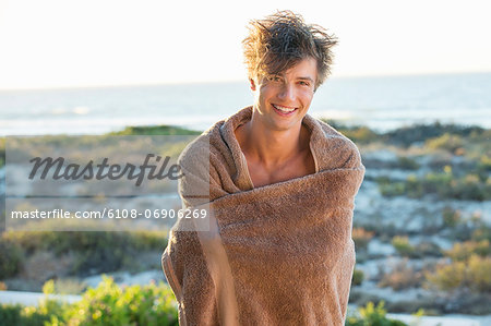 Happy man wrapped in a towel standing on the beach