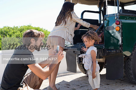 Man taking a picture of his daughter with a smartphone beside a SUV