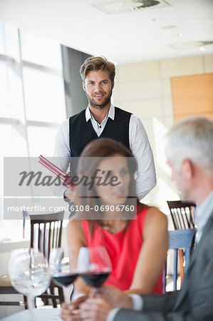 Couple enjoying red wine in a restaurant with waiter in the background