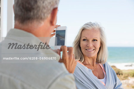 Man taking a picture of his wife with a cell phone on the beach