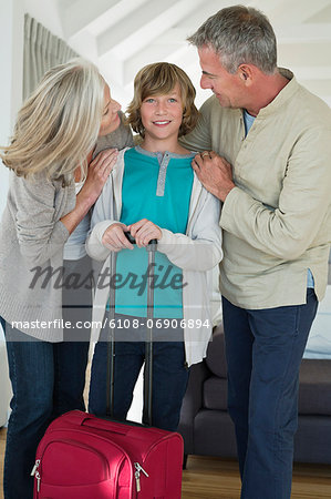 Boy holding a suitcase with his grandparents at home