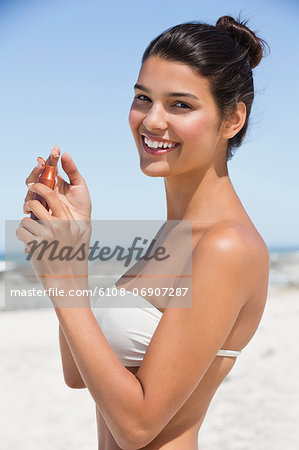 Beautiful woman holding a suntan lotion on the beach