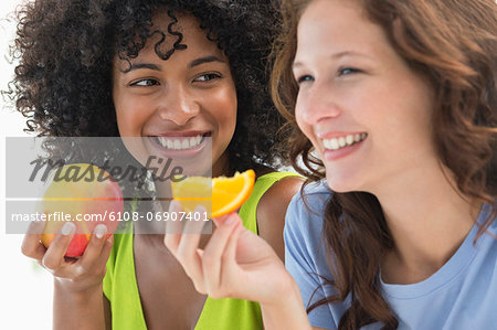 Close-up of two smiling female friends eating fruits