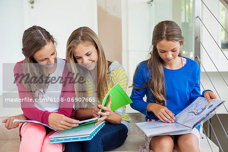 Three girls sitting on stairs and studying in a school