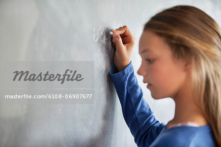 Close-up of a girl writing on a blackboard in a classroom