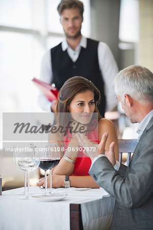 Couple discussing in a restaurant with waiter in the background