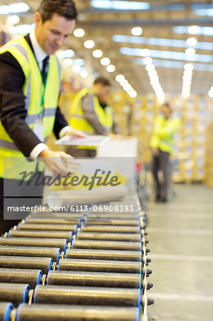 Businessman checking packages on conveyor belt in warehouse