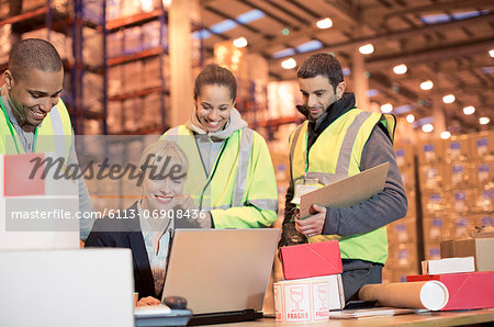 Businesswoman and workers using laptop in warehouse
