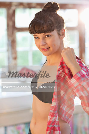 Woman putting on shirt in bedroom