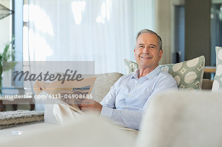 Older man reading newspaper on sofa