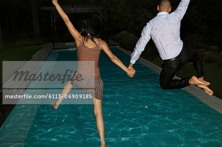 Fully dressed friends jumping into swimming pool