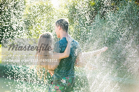 Couple playing in sprinkler in backyard