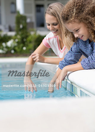 Mother and daughter dipping fingers in swimming pool