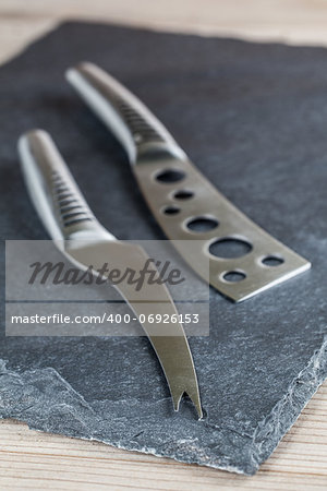 Two classy cheese knives on a slate board