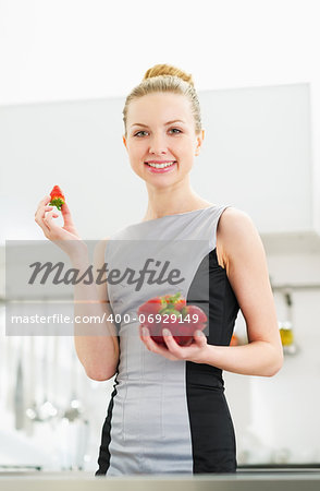 Young housewife eating strawberry in modern kitchen