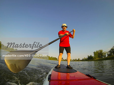 mature male paddler enjoying workout on stand up paddleboard (SUP), calm lake in Colorado, summer, distorted wide angle view