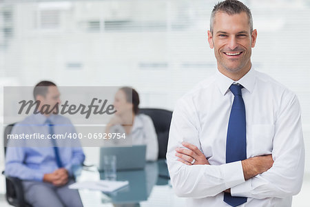 Smiling businessman posing crossing arms in bright office