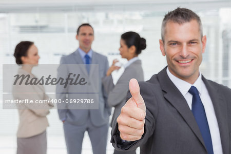 Cheerful manager showing thumb up with employees in background in bright office