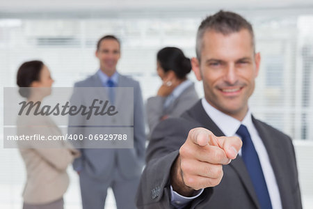 Cheerful businessman in bright office pointing at camera
