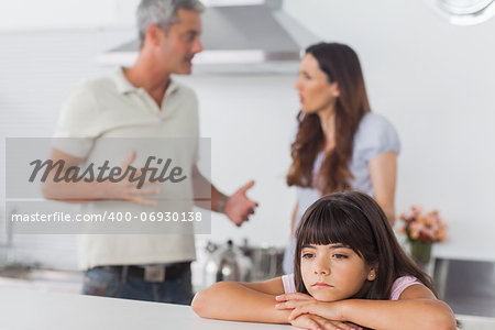 Couple having dispute in front of their unsmiling daughter sitting in kitchen at home