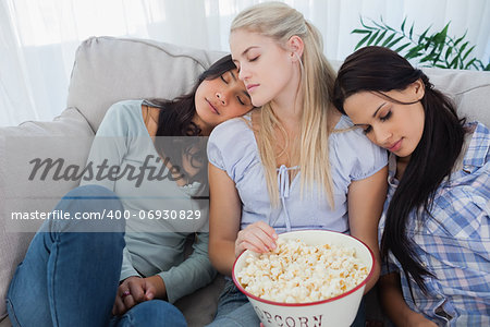 Friends dozing together on the couch while eating bowl of popcorn at home