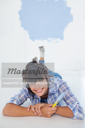 Attractive woman lying on floor holding paint brush smiling at camera