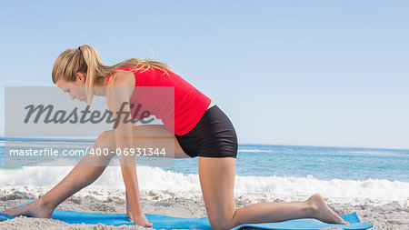 Fit blonde stretching leg on exercise mat on the beach