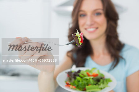 Brunette in her kitchen offering healthy salad to the camera