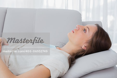 Upset brunette with a vacant look lying on the couch in her living room