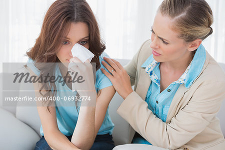 Blond therapist looking at her patient crying on sofa in office