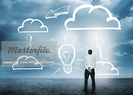 Businessman considering cloud computing graphics with light bulb in cloudy landscape