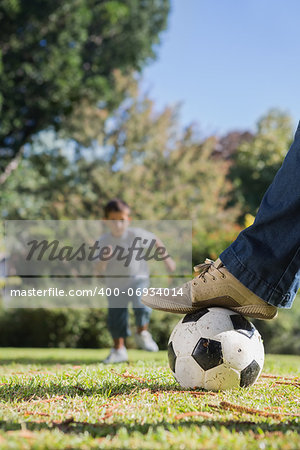 Boy running towards the football under dads foot in the park