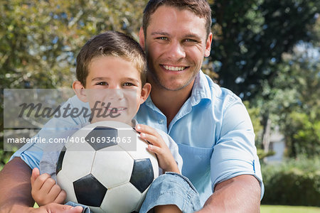 Happy dad and son with a football in a park smiling at camera
