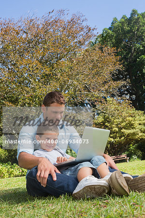 Cheerful dad and son with a laptop in a park