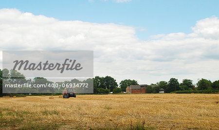 Red tractor baling cut straw in an English farm field
