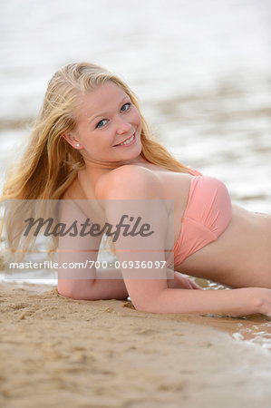 Young woman on beach at lake in summer, Bavaria, Germany.