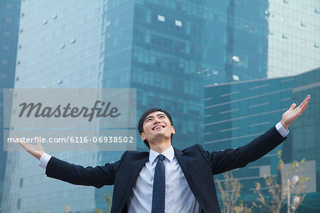 Young businessman smiling and standing outside with arms outstretched