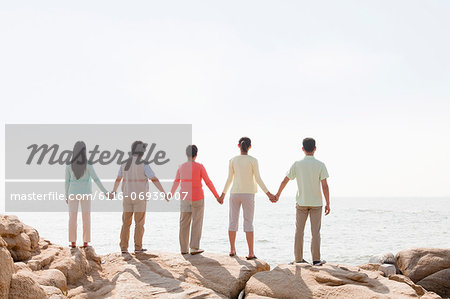 Multi-generational family holding hands on rocks by the sea, rear view