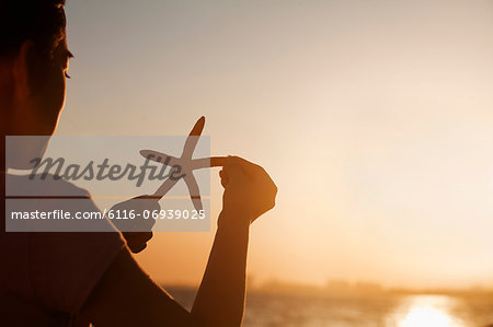 Teenage girl holding up starfish, sunset