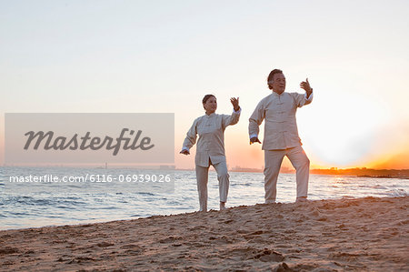 Two older people practicing Taijiquan on the beach at sunset, China