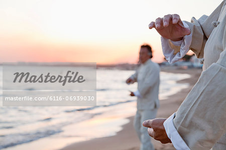 Two older people practicing Taijiquan on the beach at sunset, close up on hands